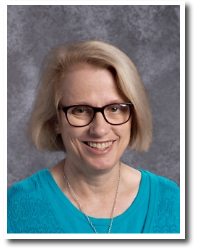 Joan Miller, Principal, short blond hair, black rimmed glasses, wearing a turquoise shirt and gold necklace