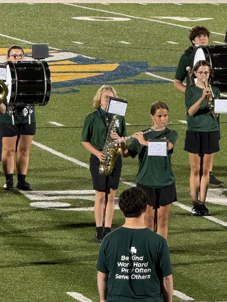 Band on the field; shirt reads Be Kind, Work Hard, Pray Often, Serve Others