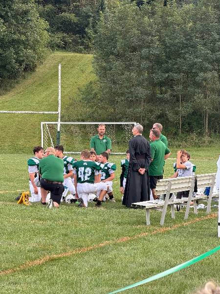 Football team huddle with coaches and Father on the home field