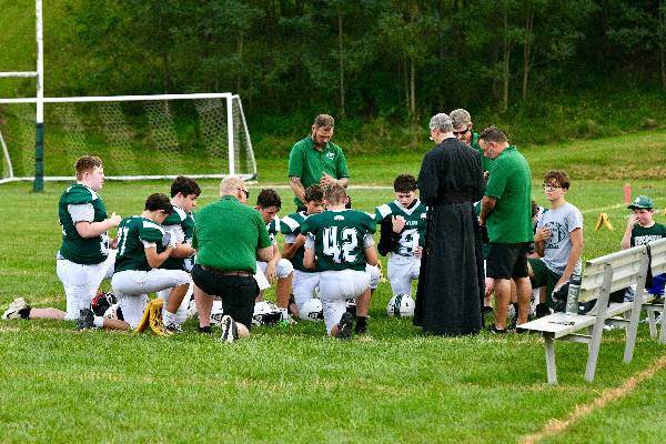 Football players kneel in prayer with Father and coaches before a game